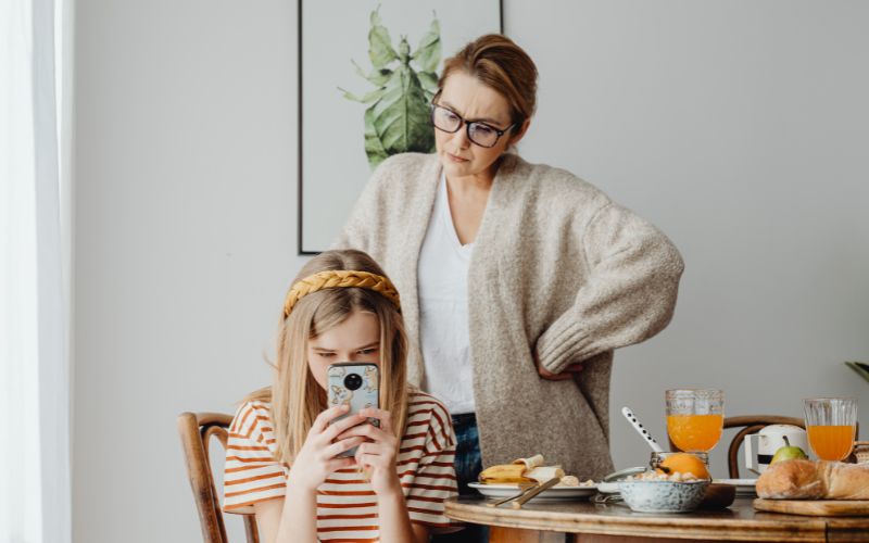 một cô gái ngồi bên bàn ăn cầm điẹn thoại yếu tố dinh dưỡng và sức khoẻ tổng thể