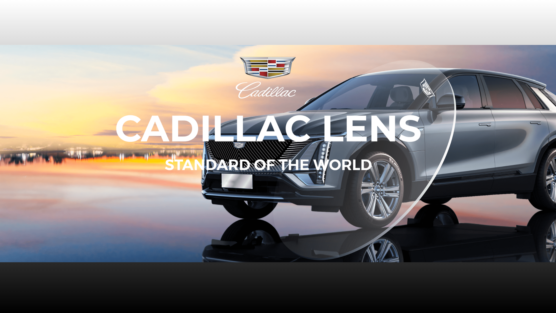 Xe SUV Cadillac màu xám đỗ bên hồ lúc hoàng hôn với logo Cadillac Lens và khẩu hiệu Standard of the World